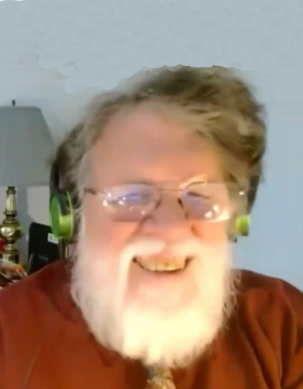 Michael Byington is a white man with grey wavy hair about two inches long and parted on one side, and a white beard covering his chin. He is wearing a burdandy shirt and a tie, with headphones and glasses, and smiling broadly.